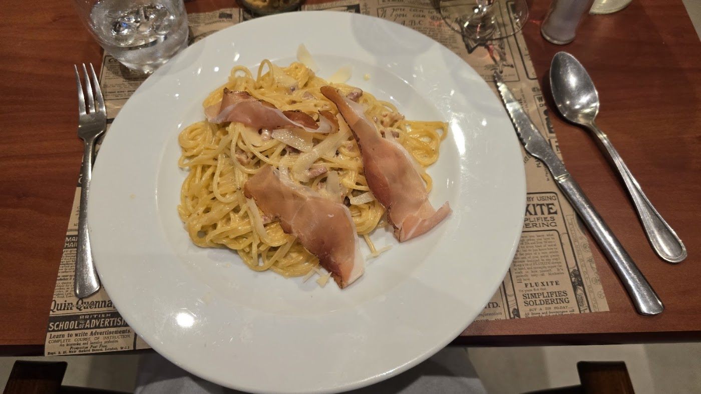 Spaghetti au jambon sec et copeaux de parmesan sur un set de table en papier journal
