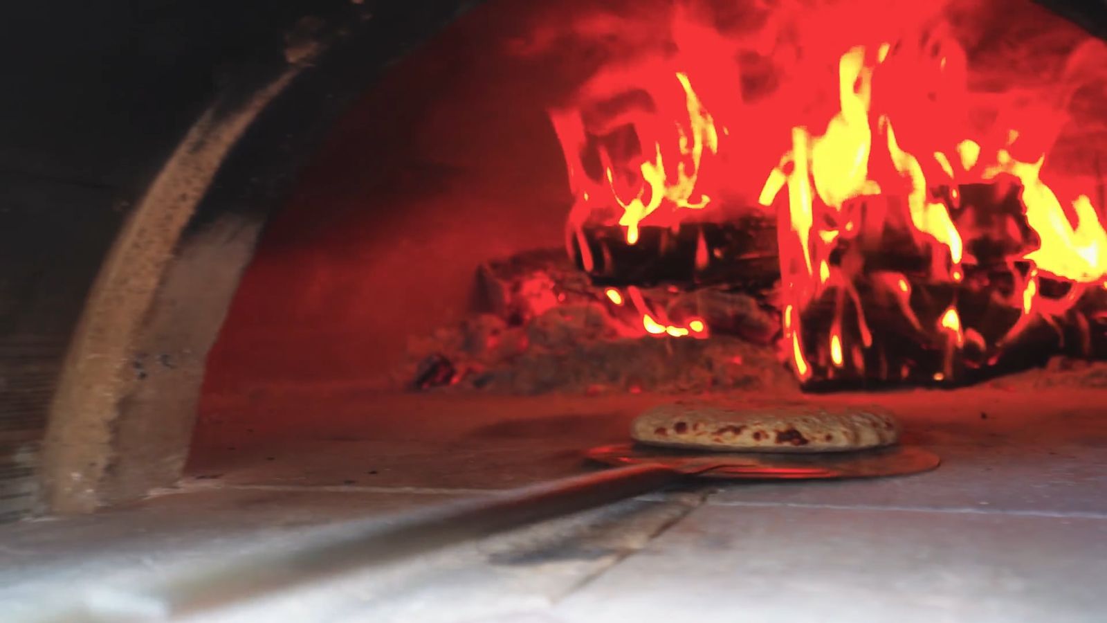 Flammes dans un four à pizza, une pizza sur la pelle